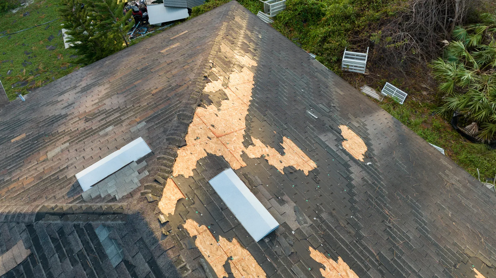 Bare decking exposed along the ridge of a shingle roof